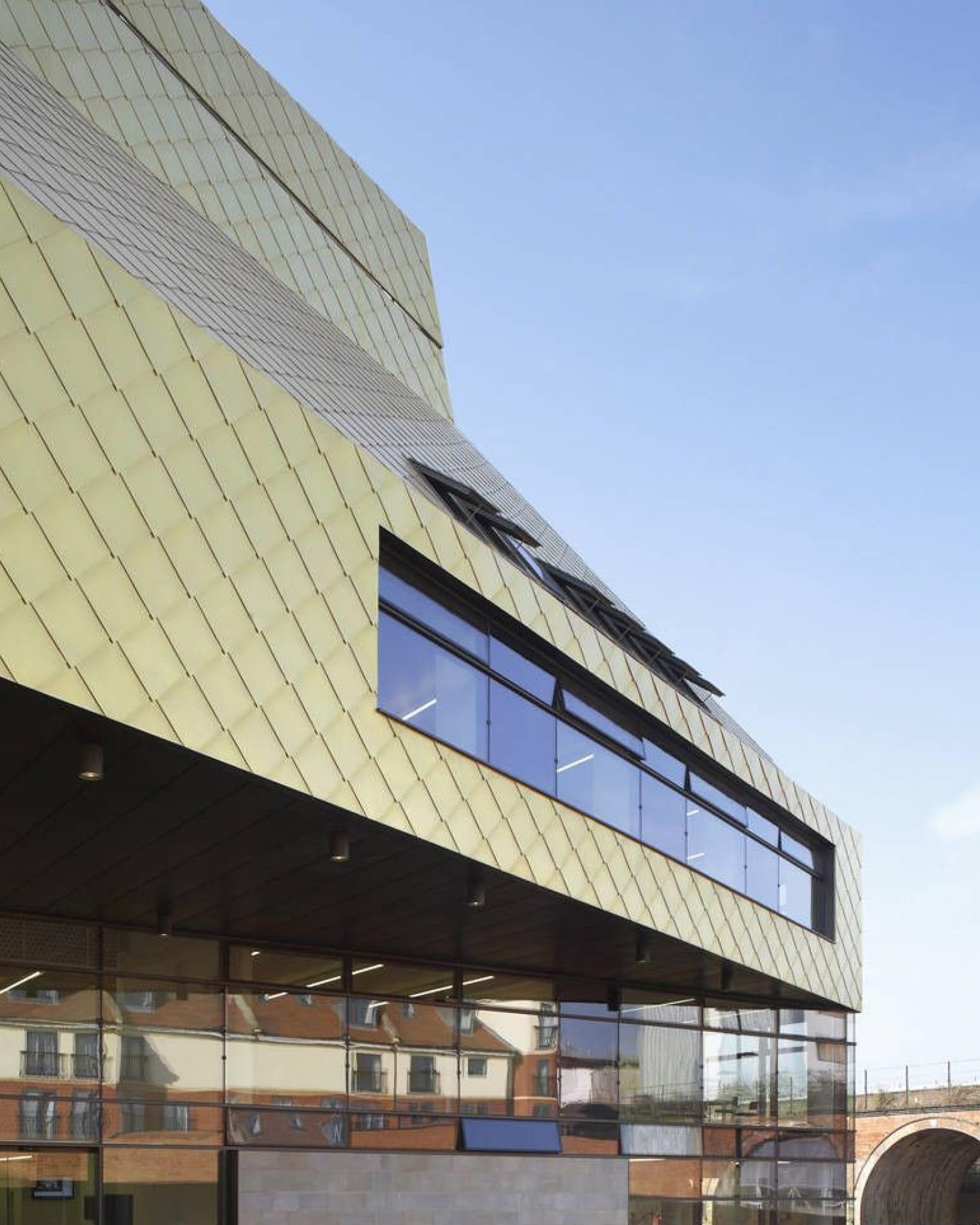 Modern building with gold, diamond-patterned exterior panels and large reflective windows under a clear blue sky.
