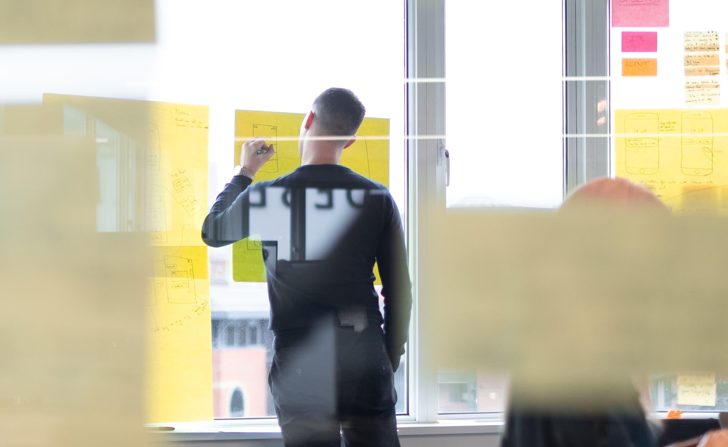 Man drawing on large yellow sticky notes on a window