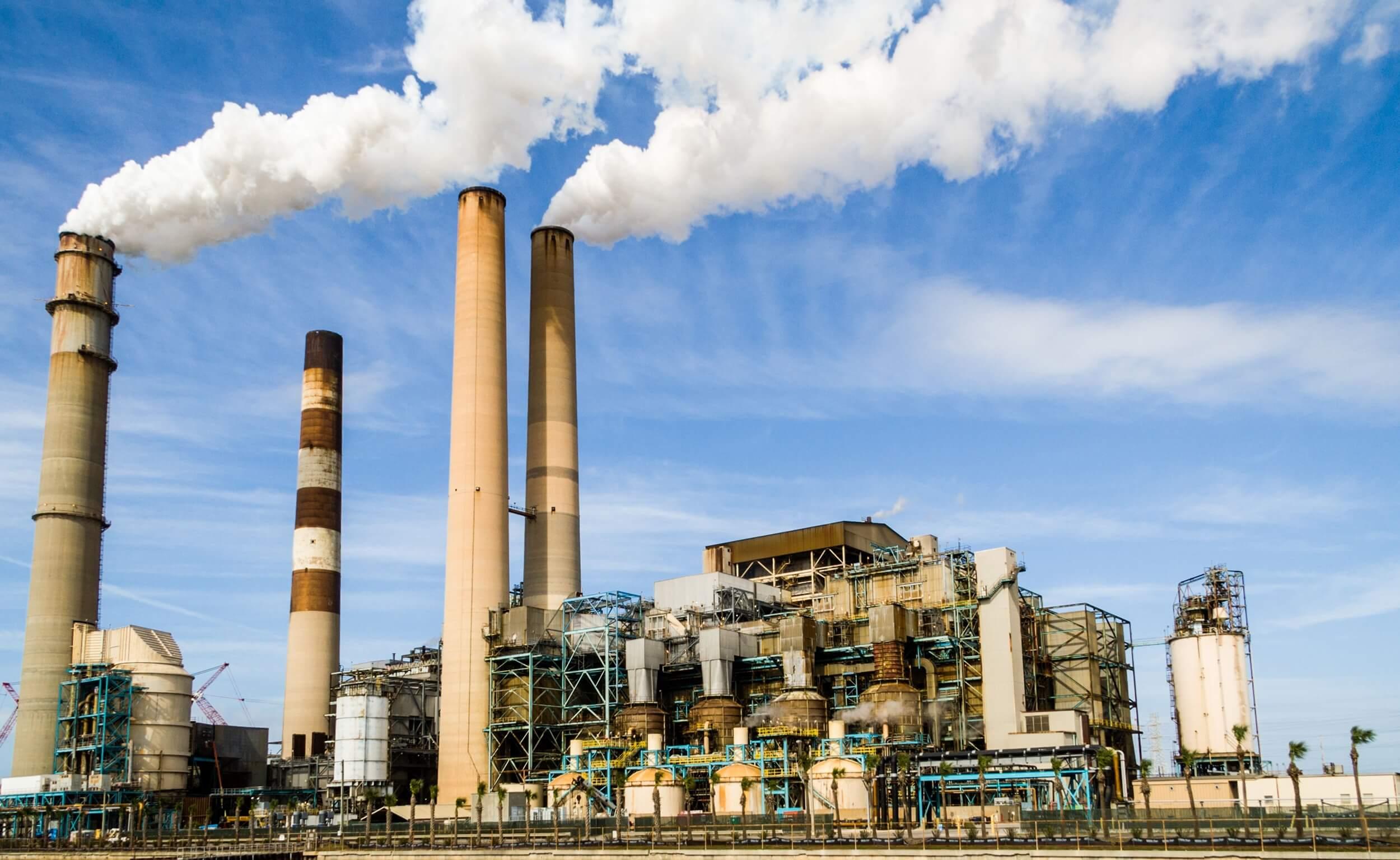 An industrial power plant with tall chimneys emitting steam against a blue sky.