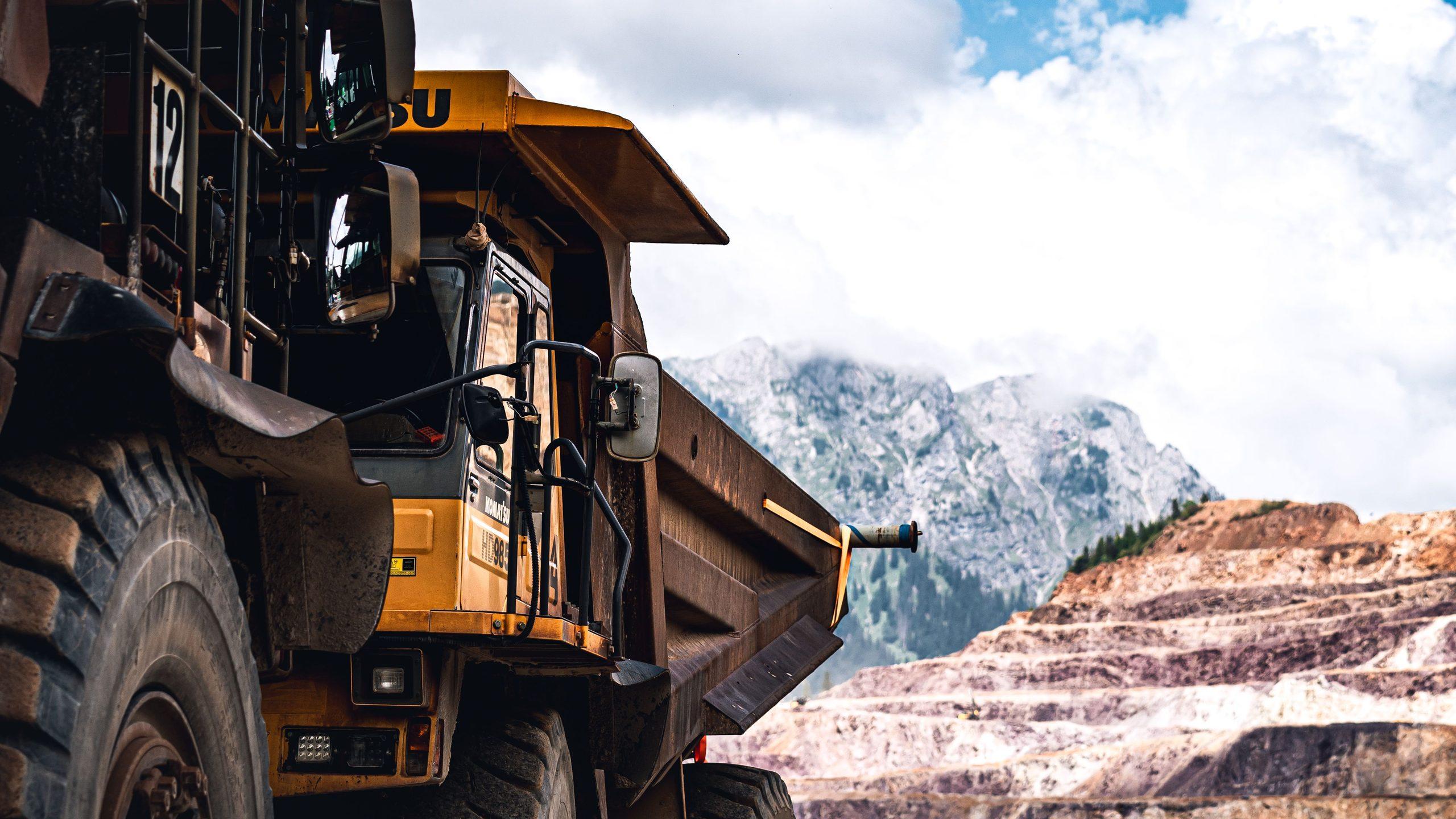 A large haul truck at an open-pit mine, with terraced rock faces and mountains behind.