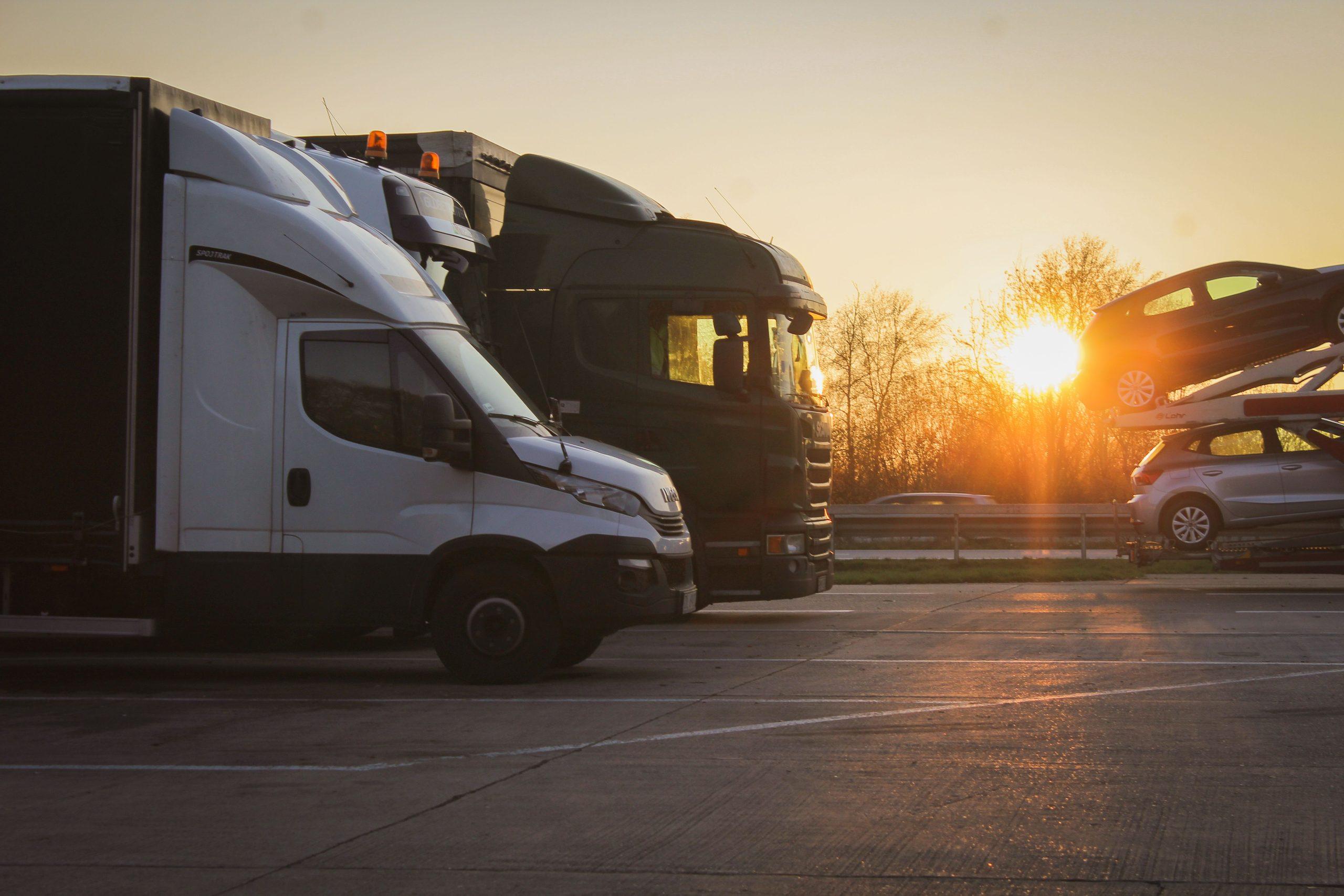 Haulage trucks and a car transporter parked at a depot at sunset.