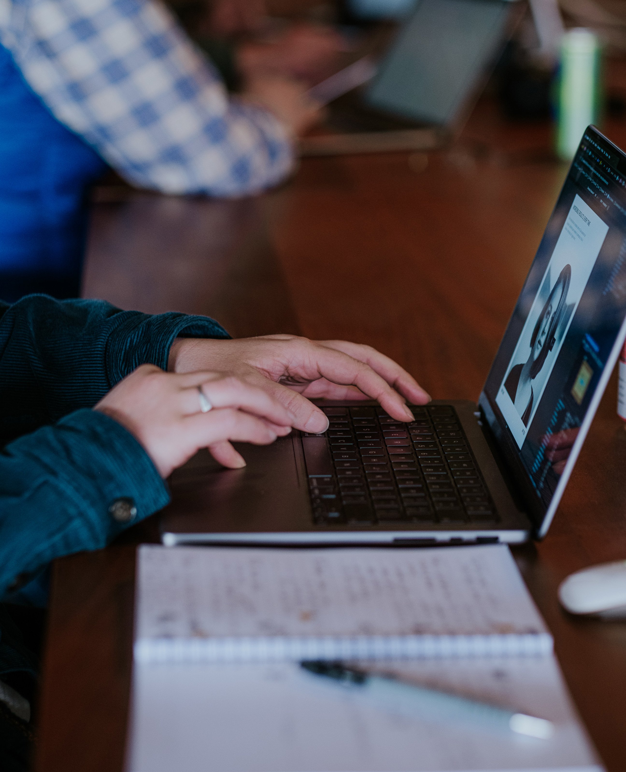 A close-up of someone typing on a laptop during a workshop, with notes and a pen on the desk.