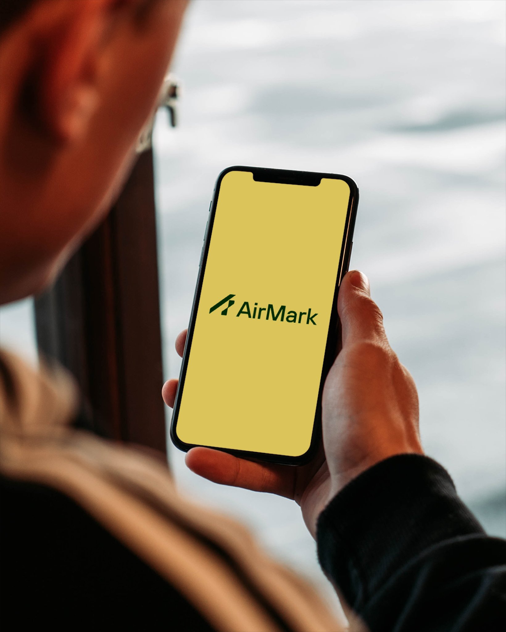 A person holding a smartphone displaying a yellow screen with the green AirMark logo.