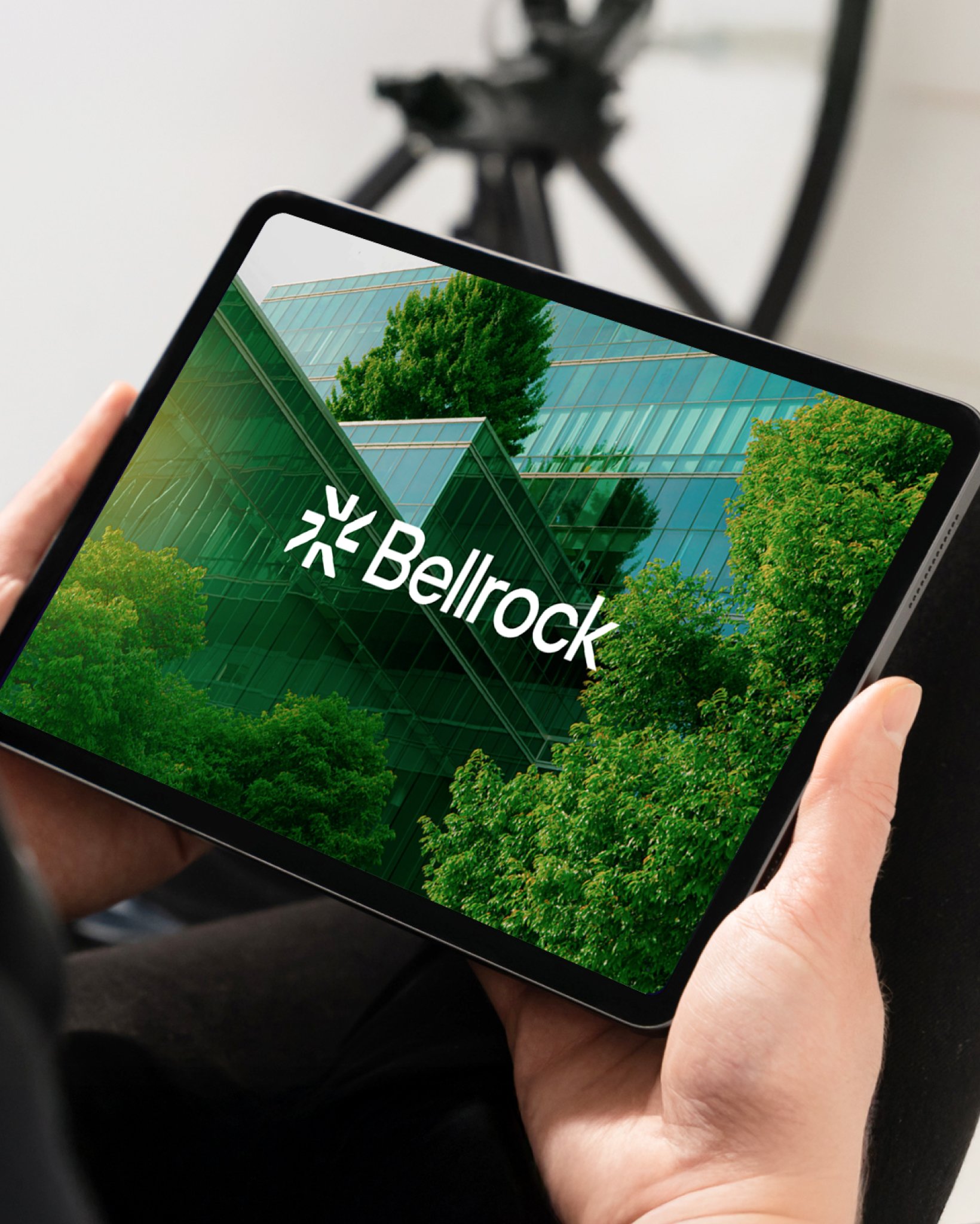 A person holding a tablet displaying the Bellrock logo over a photo of a modern glass building surrounded by green trees.