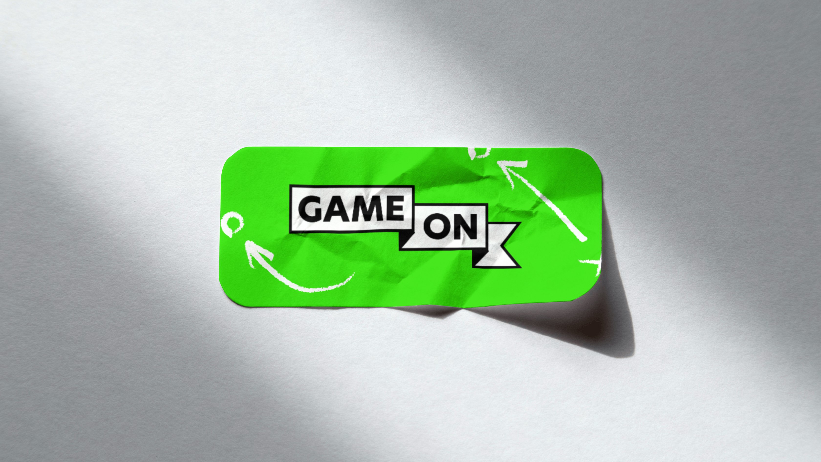A lime green 'Game On' branded card with white hand-drawn arrows, photographed against a grey background.