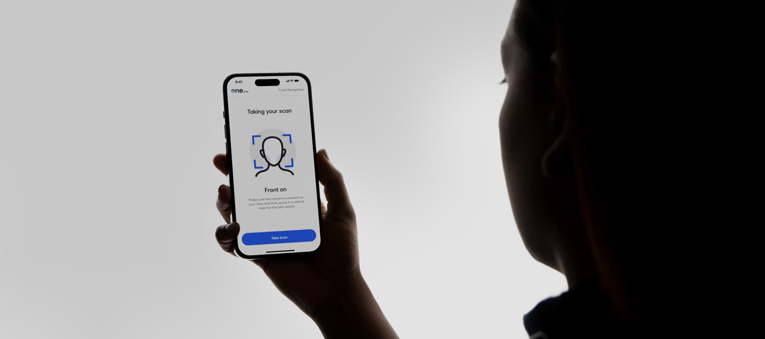A person silhouetted against a white background holds up a mobile device to scan their face for identity recognition as part of a secure login process.