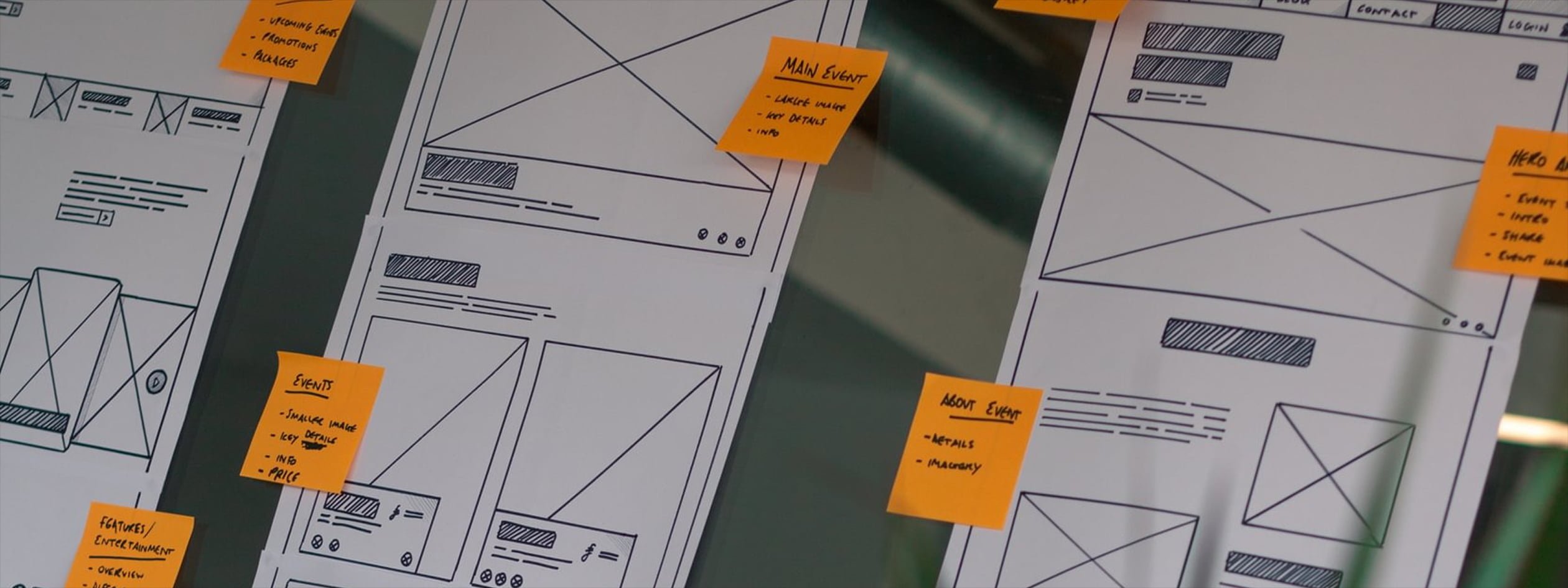 Hand drawn wireframes are displayed on a glass wall, with various sticky notes labelling key areas and thinking.