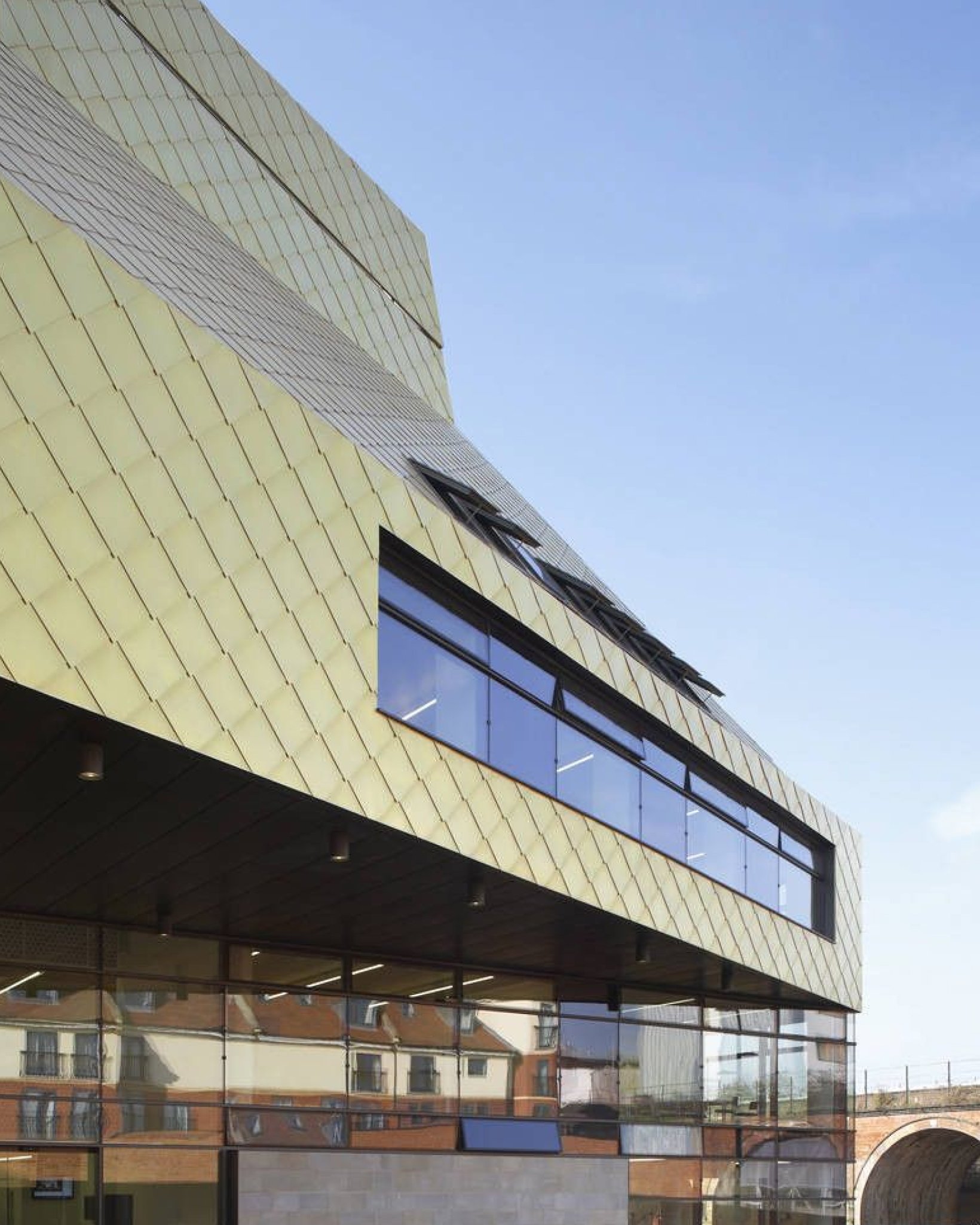Modern building with gold, diamond-patterned exterior panels and large reflective windows under a clear blue sky.