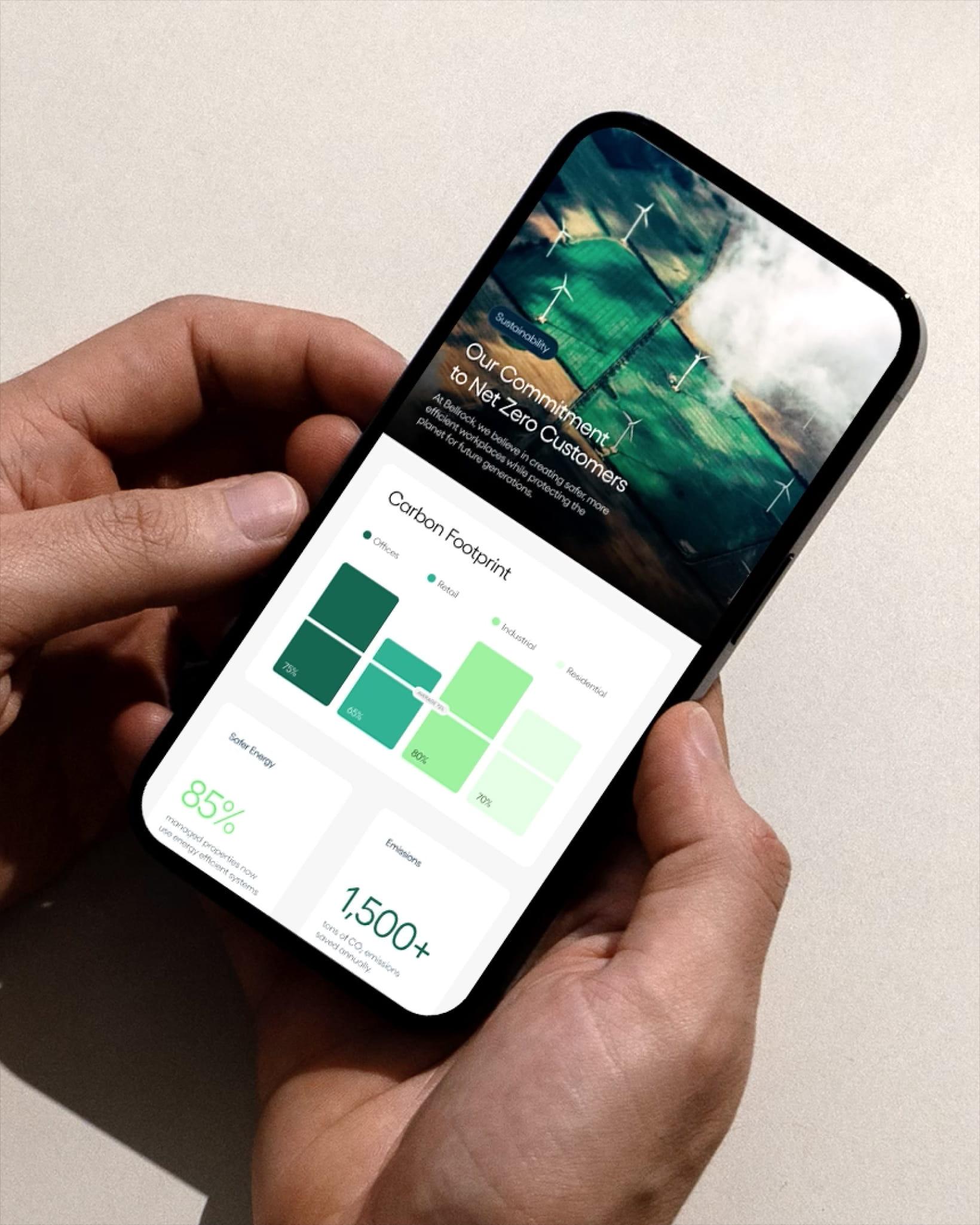 Hands holding a smartphone showing a sustainability dashboard, including a carbon footprint chart and text about a companys commitment to net-zero customers.
