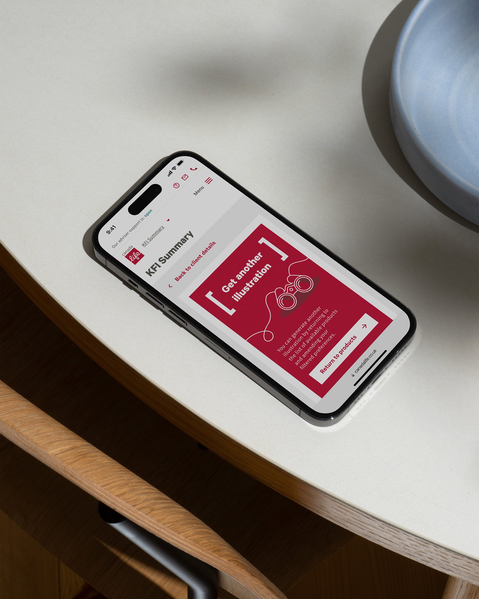 A smartphone resting on a table displaying a Canada Life KFI Summary page with a red card offering the option to get another illustration.