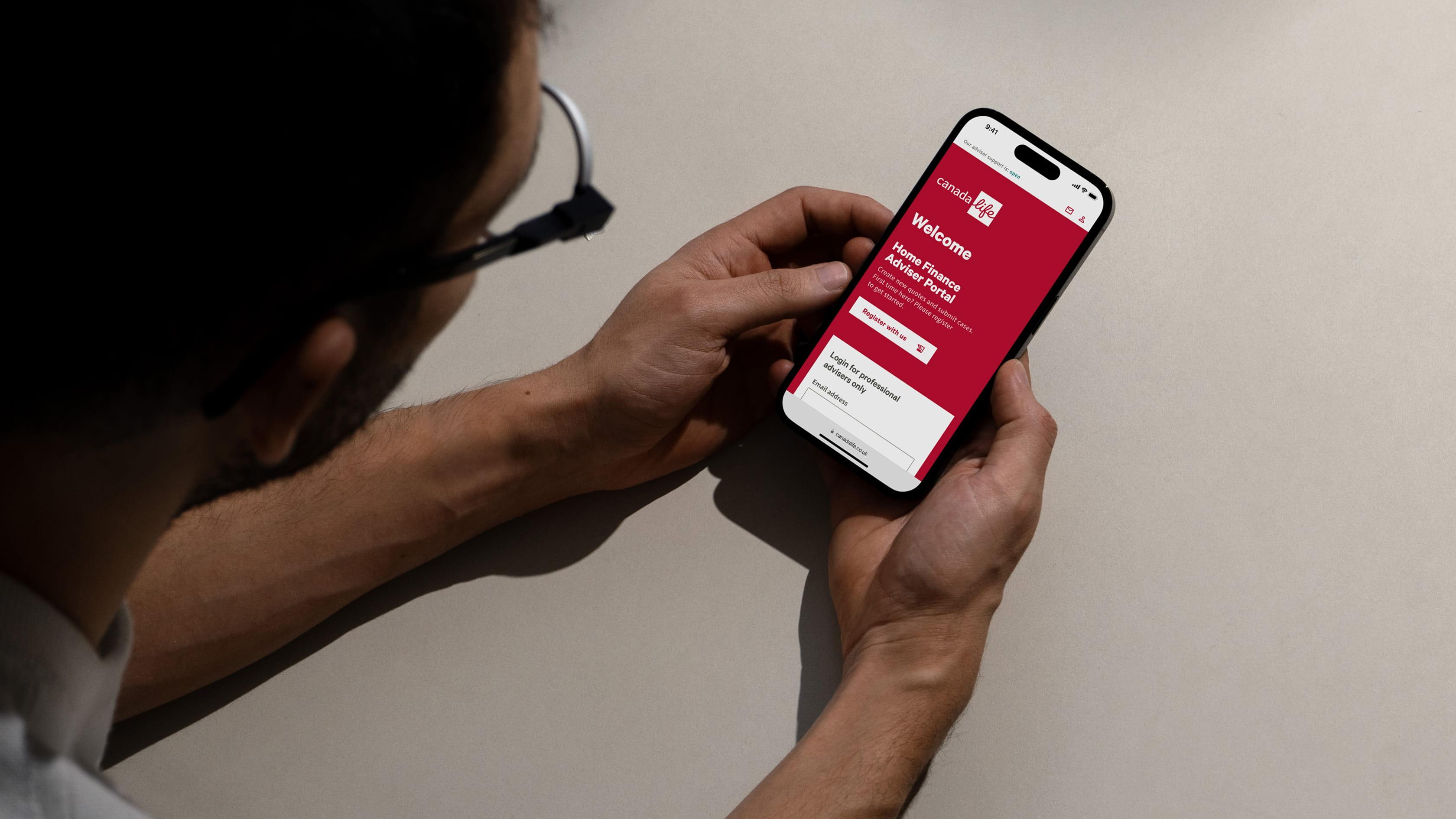 A man holding a smartphone and viewing the Canada Life Home Finance Adviser Portal welcome screen, seen from an over-the-shoulder perspective.