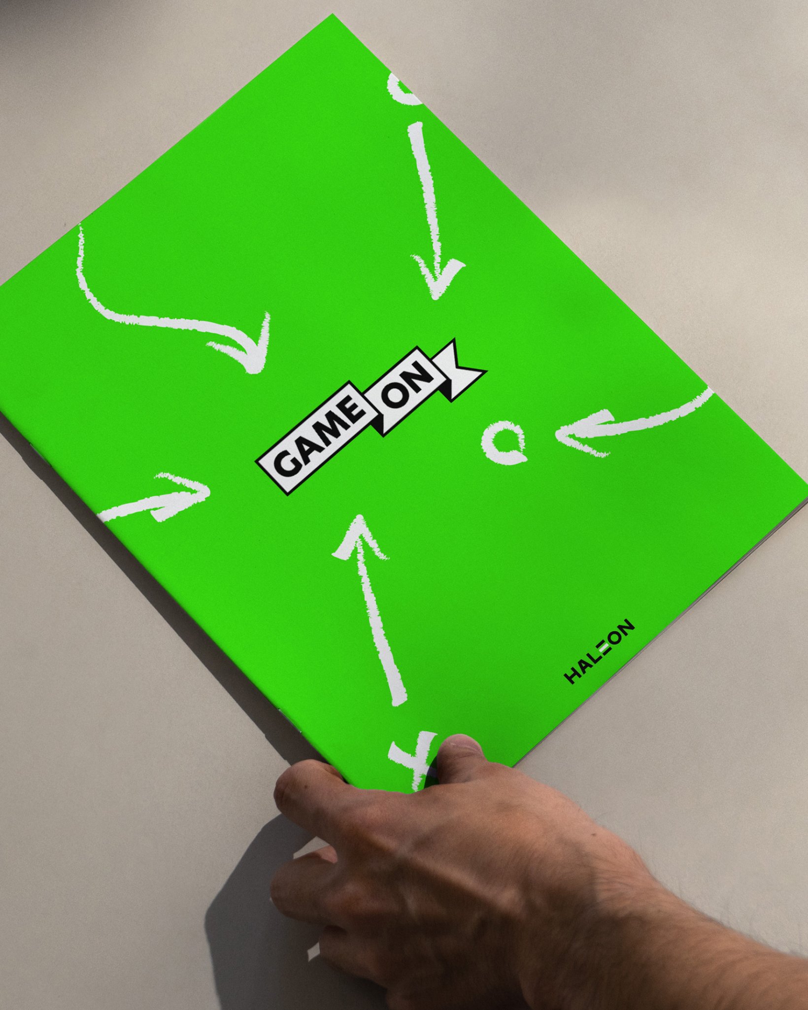 A large lime green Game On card with white hand-drawn directional arrows, held at an angle against a neutral grey background.