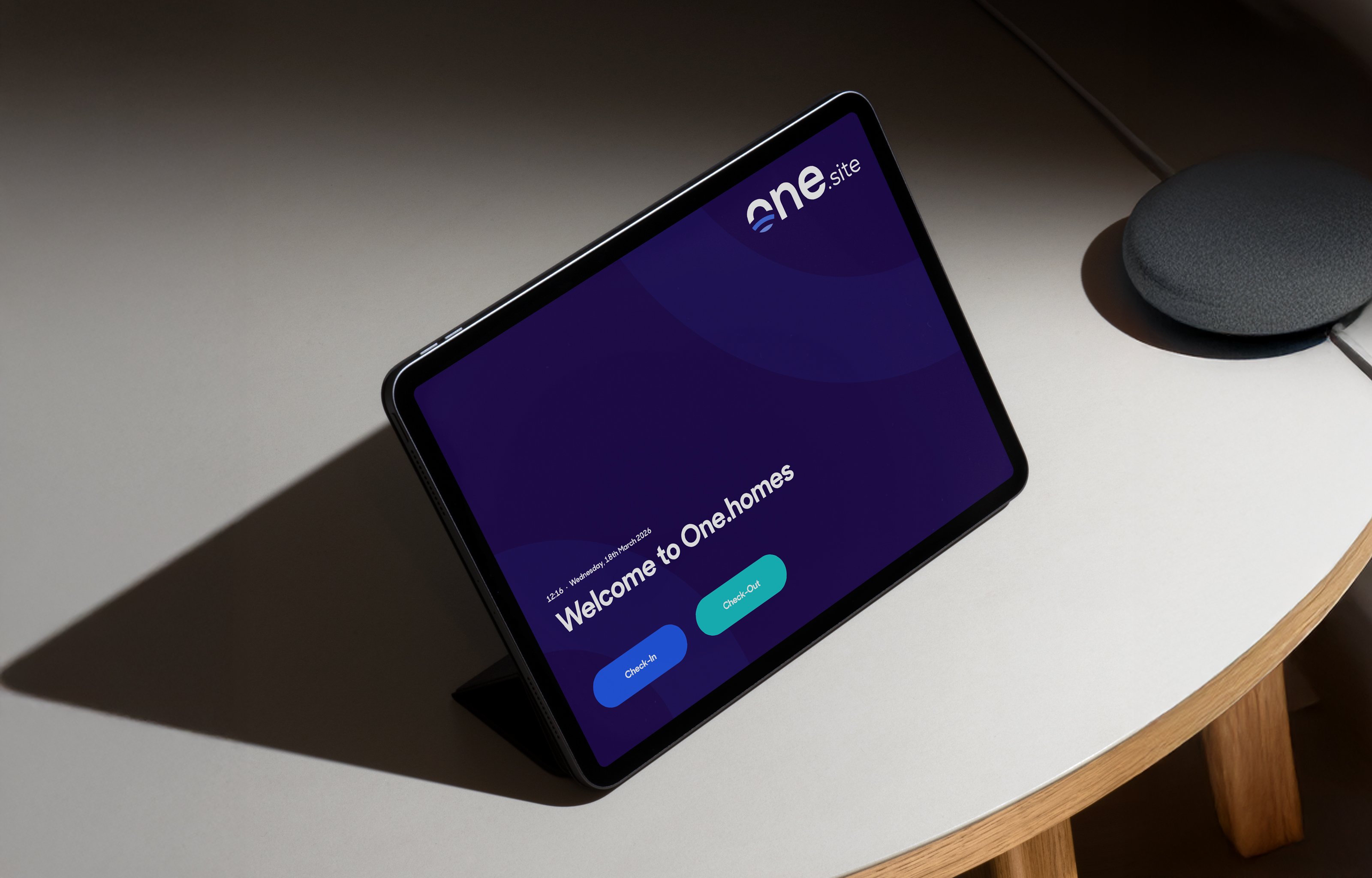 A construction worker standing at a site entrance gate being checked in via the One.site facial recognition system displayed on a mounted tablet.