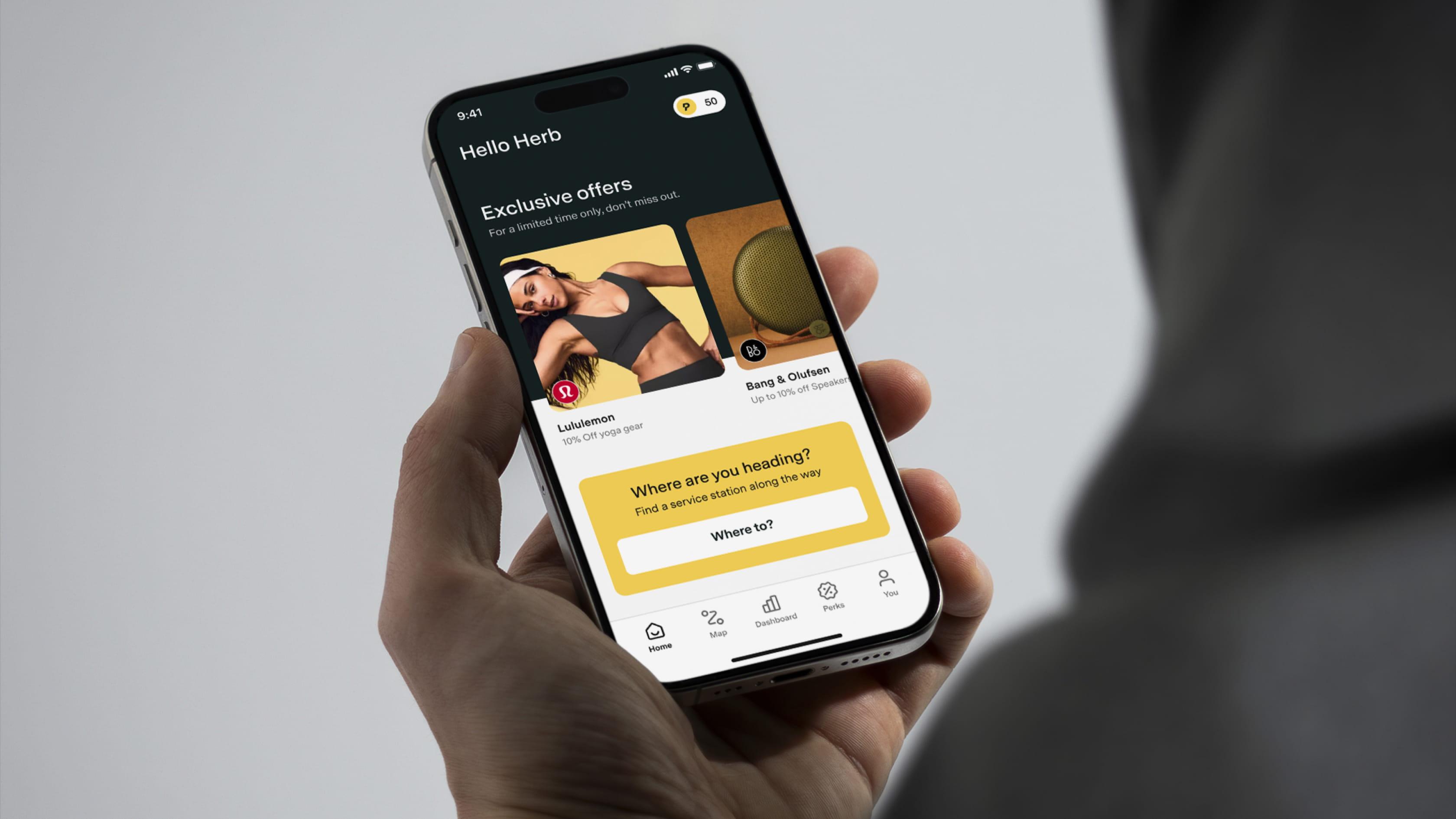 Hand holding a smartphone showing the Pitstop app home screen with exclusive offers and a search prompt asking ‘Where are you heading?'.