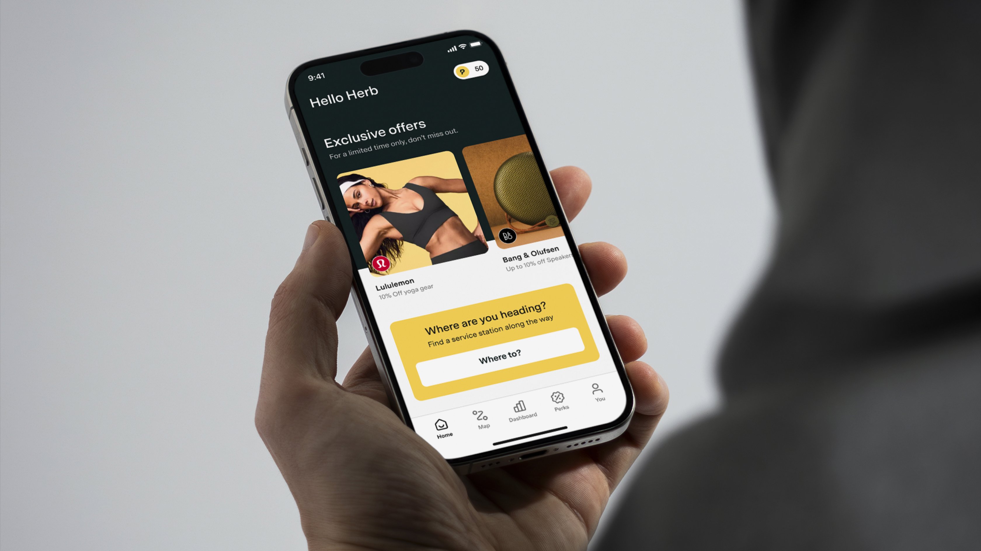 Hand holding a smartphone showing the Pitstop app home screen with exclusive offers and a search prompt asking ‘Where are you heading?'.