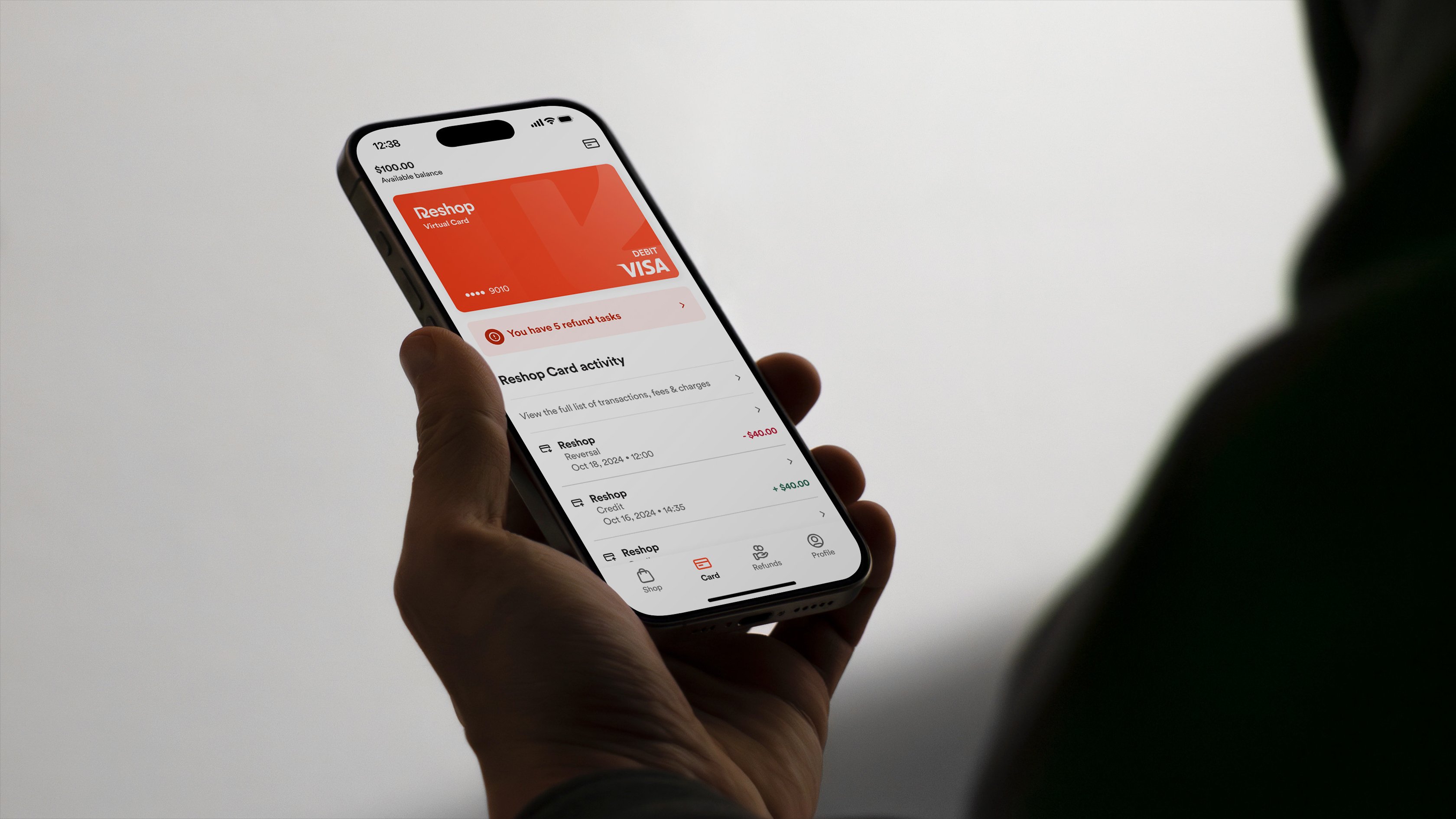 A silhouetted man holds up a mobile device displaying the ReShop app in use. Recent payments activity is listed beneath a selected payment method.