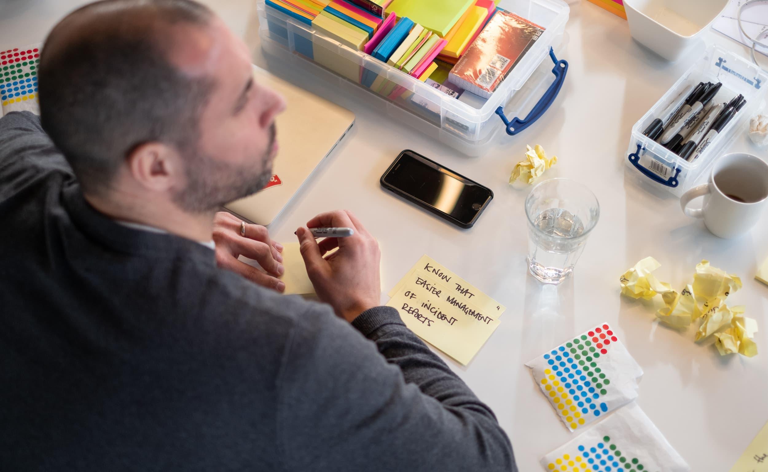 Man writing sticky-note at a messy workshop table.