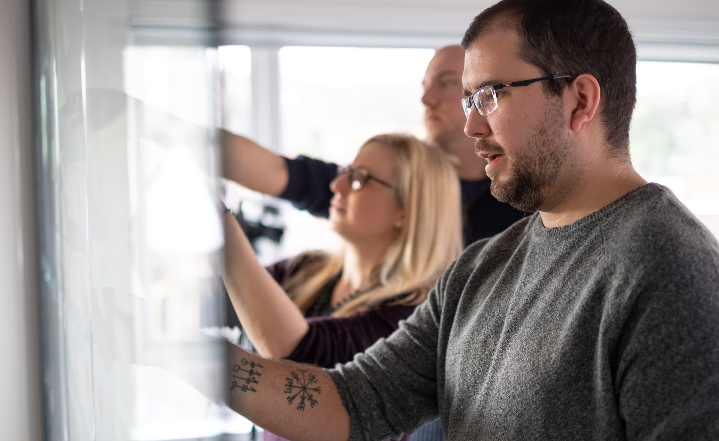 Team at a whiteboard placing sticky notes (Harry + Zoë)