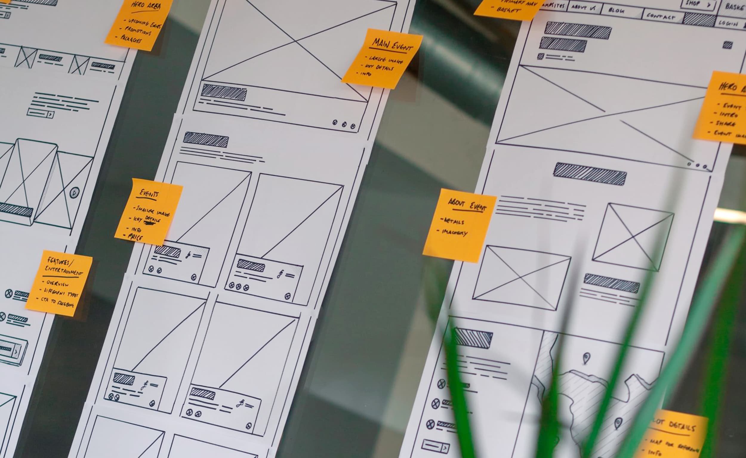 Hand drawn wireframes are pinned up on a glass wall, with orange post it notes stuck on top that highlight key areas and considerations