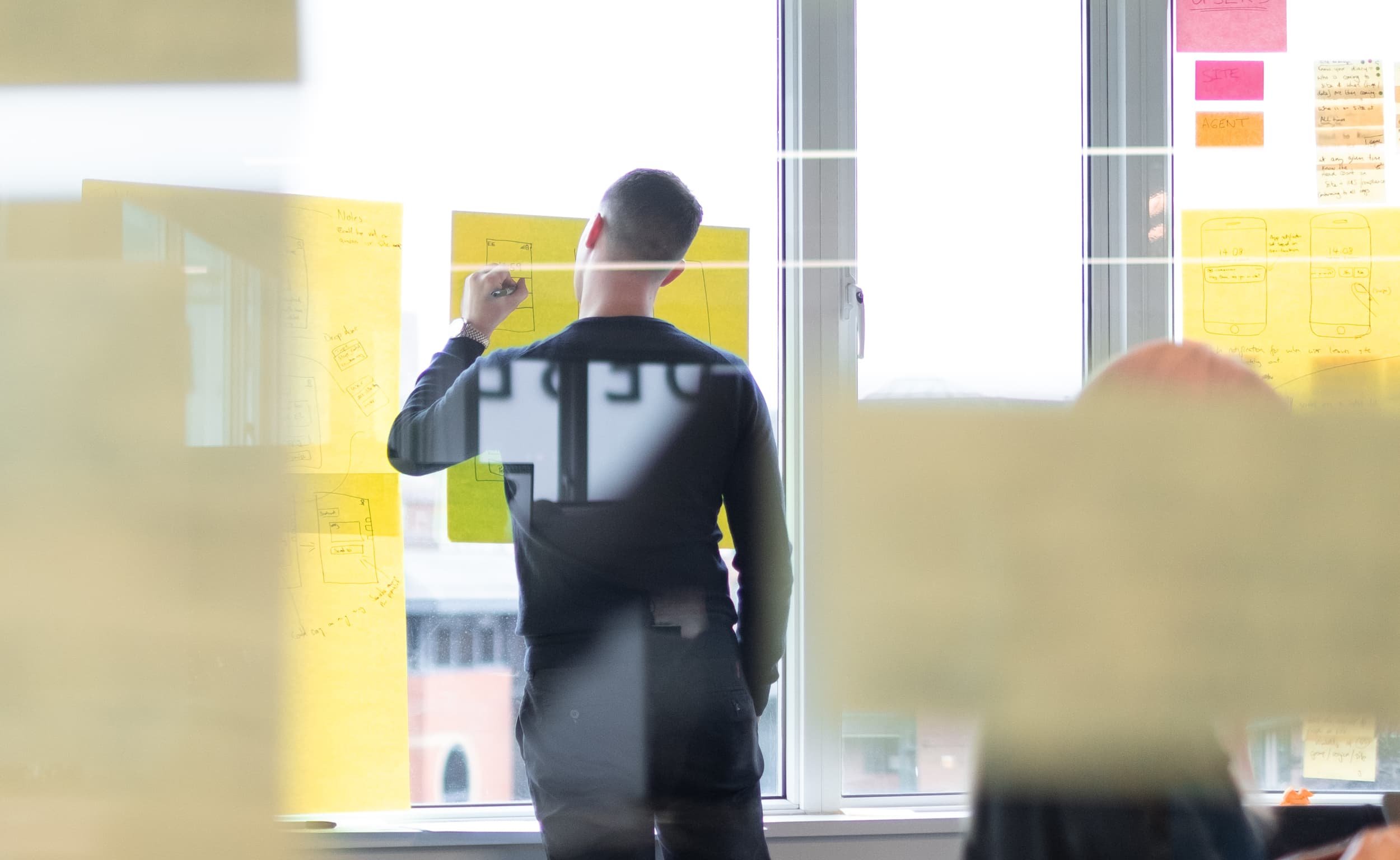 Man drawing on large yellow sticky notes on a window