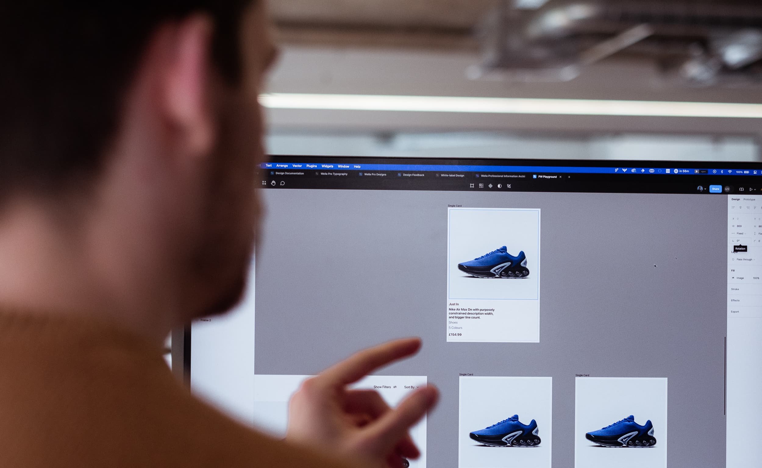 Designer pointing at screen showing product cards with blue trainers