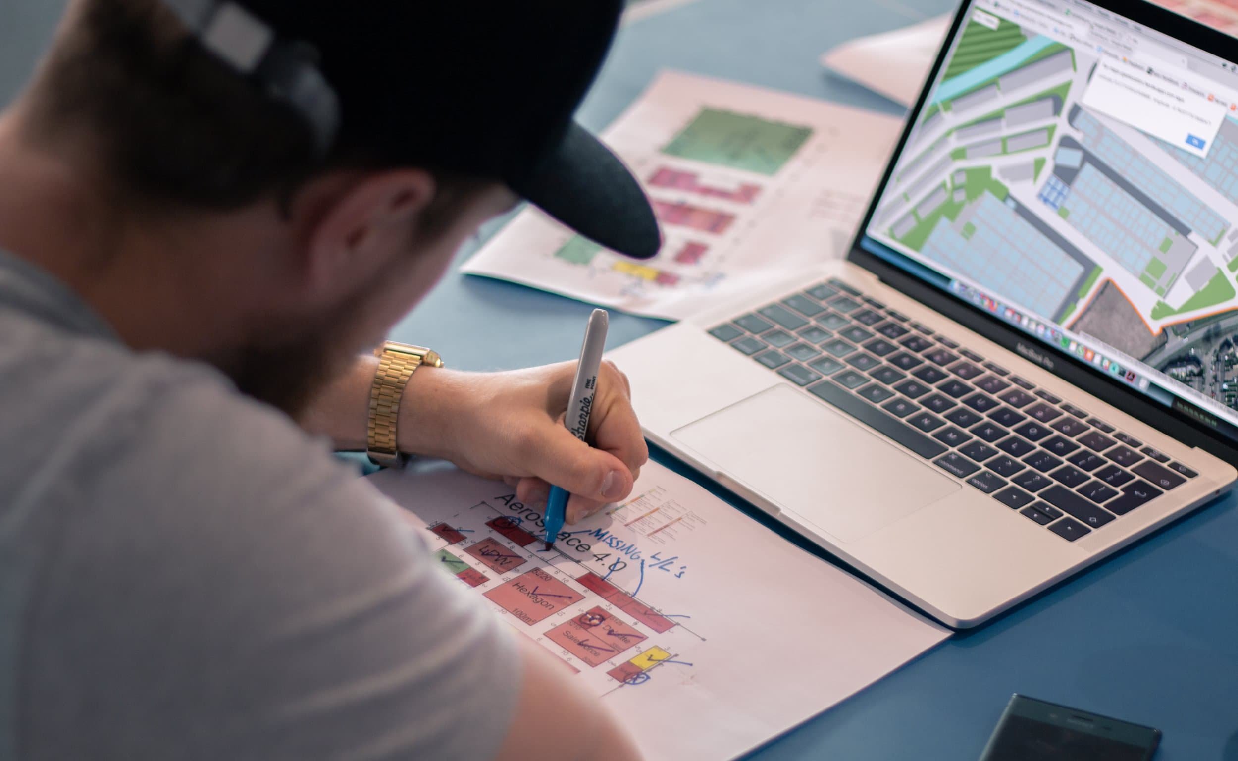Person sketching coloured site plans next to a laptop