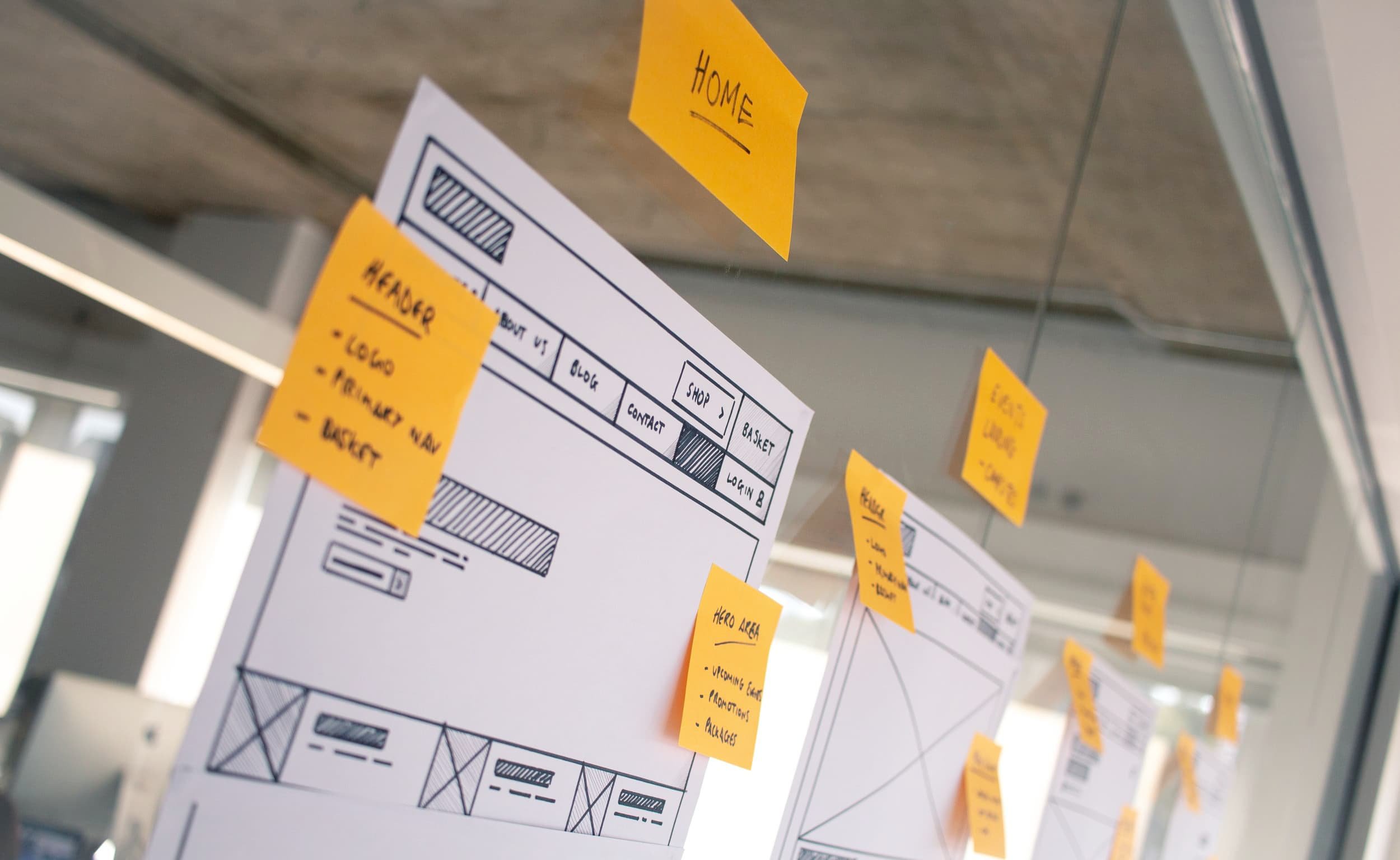 Yellow sticky notes + wireframes on glass (close-up with “HOME”)